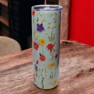 Może przedstawiać: Jasnoniebieski kubek ze stali nierdzewnej z nadrukiem kwiatowym z prasowanymi kwiatami w odcieniach czerwonego, żółtego, fioletowego i białego.
