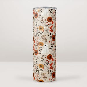 Pode incluir: Um copo de aço inoxidável branco com um padrão floral de outono e um design de fantasma. O padrão apresenta flores laranja, vermelhas e amarelas com folhas verdes sobre um fundo creme.
