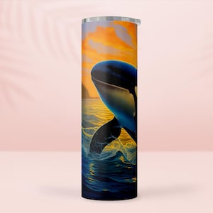 Może przedstawiać: Cylindryczny kubek z żywą ilustracją orki wynurzającej się z oceanu. Projekt przedstawia czarno-białą orkę na tle zachodu słońca z pomarańczowymi i żółtymi odcieniami. To naczynie do picia.