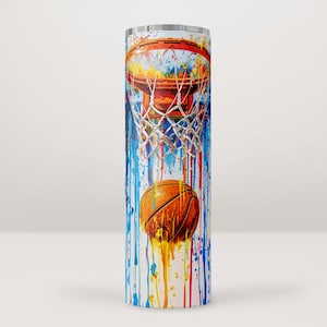 Pode incluir: Um copo alto e cilíndrico com tema de basquete. O design apresenta uma bola de basquete passando por uma cesta, com respingos de tinta coloridos em vermelho, laranja, amarelo, azul e branco. O copo é provavelmente feito de aço inoxidável.
