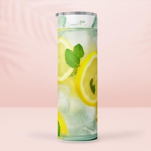 Pode incluir: Um copo alto e cilíndrico com uma bebida refrescante com rodelas de limão, gelo e folhas de hortelã. O design evoca uma bebida de verão fresca. O copo tem uma tampa prateada e um padrão verde claro e branco.