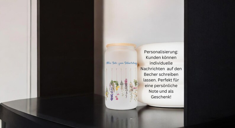 May include: A white frosted glass jar with a bamboo lid. The jar has a floral design with the text "Mir Danke zum Geburtstag" on the front. The jar is sitting on a black shelf. The text "Personalisierung: Kunden k&ouml;nnen individuelle Nachrichten auf den Becher schreiben lassen. Perfekt f&uuml;r eine pers&ouml;nliche Note und als Geschenk!" is visible on the right side of the image.