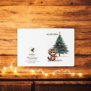 May include: A white card with a cute cartoon cat wearing a red scarf and a wreath of flowers, standing next to a Christmas tree with red ornaments and lights. The text "Winter Lights" is at the top of the card. The text "Parissahandmade" is at the bottom of the card.