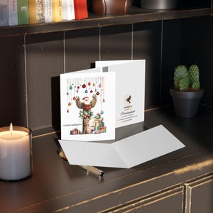 May include: A Christmas card featuring a watercolor illustration of an owl wearing a Santa hat and holding ornaments. The owl is perched on a tree stump with presents stacked underneath. The card has the text "Frohe Weihnachten" printed on the front.