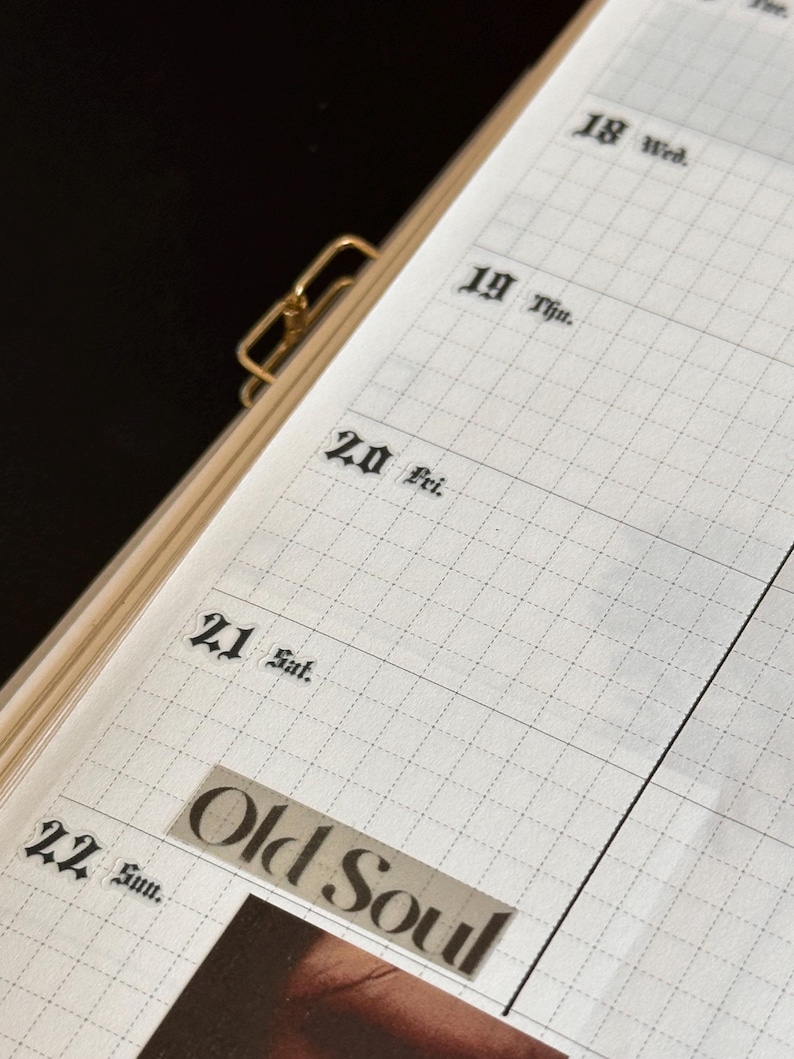May include: Open planner with grid-lined pages, featuring dates and the words "Old Soul" on a sticker. The planner is held together with a gold-coloured clip. The dates of the week are printed in a classic font.