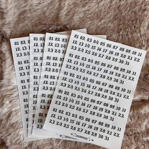 May include: A stack of small white paper sheets with black text, featuring dates like "01 02 03" and "12 13 14", rests on a textured, light brown surface. The sheets are labelled "LoveSophiee".
