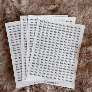 May include: Several white paper sheets with a repeating pattern of days of the week in a grid. The text is in black. The sheets are on a textured, light brown surface. The bottom sheet has the text "LoveSophiee".