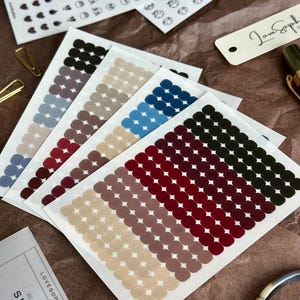 May include: A collection of sticker sheets featuring small, colorful dot stickers in various shades of blue, red, brown, and green. Additional sheets display small face and heart designs. The text "SMALL DOTS" is visible on one sheet.