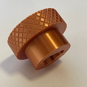 May include: A 3D printed, copper-colored, round knob with a textured surface and a keyhole.
