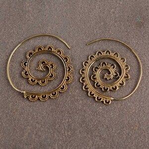 May include: A pair of gold-coloured spiral earrings. Each earring has a central spiral design with a decorative, scalloped edge. The earrings are shown against a neutral, grey background.