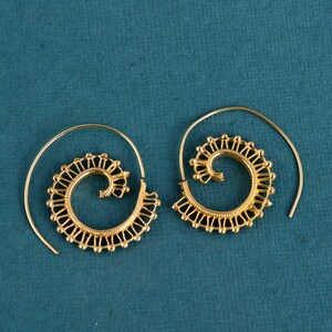May include: A pair of gold spiral earrings. Each earring has a spiral design with a decorative edge and a wire hook. The earrings are presented against a teal background.