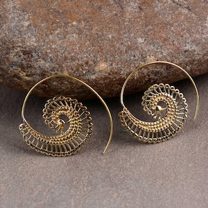 May include: A pair of gold-coloured spiral earrings. Each earring has a detailed, openwork design with a spiral shape and a delicate, lacy edge. The earrings are displayed on a neutral, textured surface.
