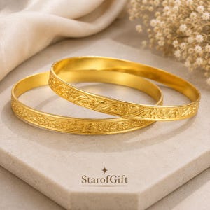 May include: Two gold-colored bangles featuring an embossed floral and vine pattern along the outer surface. The bracelets have a smooth, polished interior and a rounded profile. The text StarofGift is printed below the jewelry pieces.