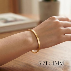 Może przedstawiać: Polerowana bransoletka typu bangle w kolorze złotym z gładką, płaską powierzchnią i mechanizmem zapięcia na zawiasach. Bransoletka ma szerokość 4 mm, co wskazuje tekst SIZE: 4MM wydrukowany w prawym dolnym rogu obrazu.