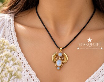 May include: A gold-toned pendant featuring a winged scarab design with three iridescent moonstone cabochons, suspended from a black braided cord necklace. The pendant displays intricate metalwork and the text STAROFGIFT JEWELRY MADE TO STAND OUT.