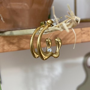May include: Gold hoop earrings with an irregular, abstract shape and a small pearl accent.