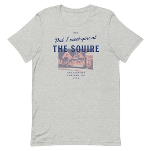 May include: A light gray t-shirt featuring the text "Did I meet you at THE SQUIRE" above a vintage-style image of a building. Below the image, the text reads "THE EIGHTIES CHATHAM, MA U.S.A" in a retro font.