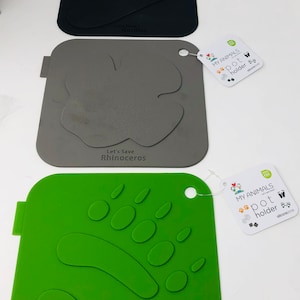 May include: Three silicone pet food mats in black, gray, and green. Each mat features an animal footprint design and the text "Let's Save" followed by the animal's name. The mats have a small hole for hanging and a tag that reads "MY ANIMALS pot holder."