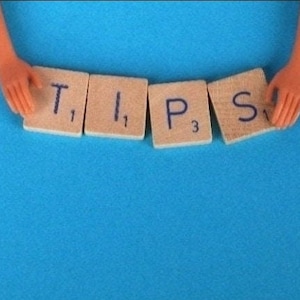 May include: The word "TIPS" spelled out using letter tiles on a blue background. The tiles are brown with white lettering and black numbers.