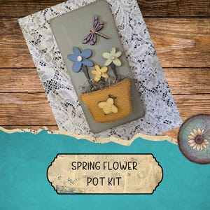 May include: A decorative spring flower pot kit with a gray background, featuring a fabric pot with a yellow bee, and wooden flowers in blue, yellow, and green. A wooden dragonfly and lace are also included. The text "Spring Flower Pot Kit" is displayed.
