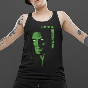 May include: A person wearing a black tank top with the text "I'm the Green Man" and a green image of a man's face. The person is also wearing a black bucket hat and black shorts.