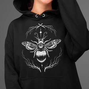 May include: Black hooded sweatshirt with a white graphic of a bee with a single eye and intricate floral designs.