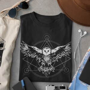 K&ouml;nnte beinhalten: Schwarzes T-Shirt mit einem wei&szlig;en geometrischen Design, das eine Eule im Flug zeigt. Das Design beinhaltet einen Kreis, ein Dreieck und andere geometrische Formen.