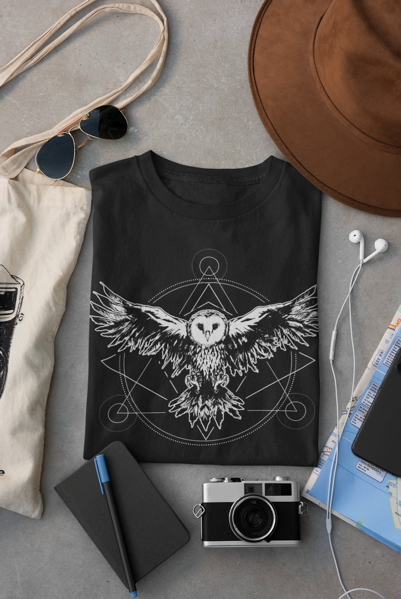 K&ouml;nnte beinhalten: Schwarzes T-Shirt mit einem wei&szlig;en geometrischen Design, das eine Eule im Flug zeigt. Das Design beinhaltet einen Kreis, ein Dreieck und andere geometrische Formen.
