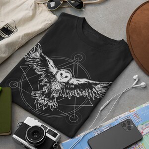 K&ouml;nnte beinhalten: Schwarzes T-Shirt mit einem wei&szlig;en Aufdruck einer Eule, die in einem geometrischen Muster fliegt.