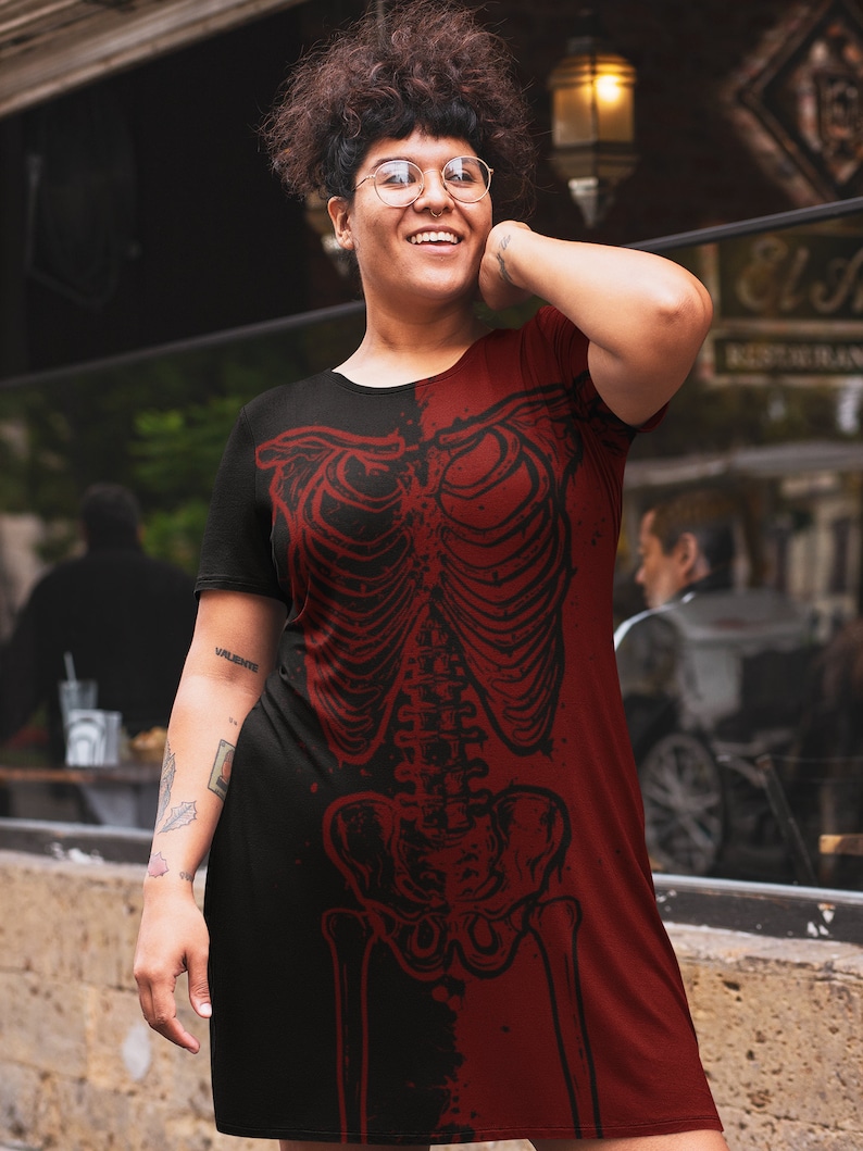 K&ouml;nnte beinhalten: Ein schwarzes und rotes T-Shirt-Kleid mit einem Skelett-Grafikdruck. Das Skelett ist in roter Farbe und auf der rechten Seite des Kleides gedruckt. Die linke Seite des Kleides ist schwarz.