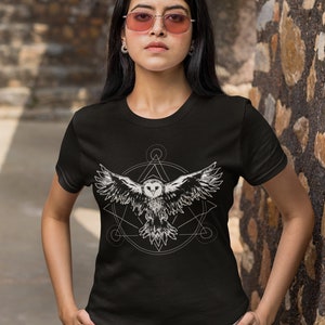 K&ouml;nnte beinhalten: Schwarzes T-Shirt mit einem wei&szlig;en Grafikdruck eines fliegenden Eulen innerhalb eines geometrischen Designs.
