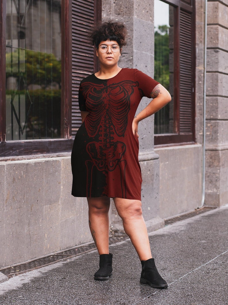 K&ouml;nnte beinhalten: Eine Frau tr&auml;gt ein weinrotes Kleid mit einem schwarzen Skelett-Druck. Sie steht vor einem Geb&auml;ude mit einem Fenster und einer Backsteinmauer. Sie tr&auml;gt schwarze Stiefeletten.