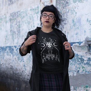 May include: Black t-shirt featuring a white graphic of a woman with antlers and a crescent moon on her head. The graphic is surrounded by stars.
