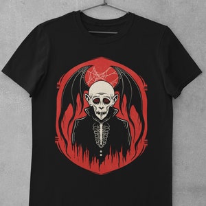 K&ouml;nnte beinhalten: Schwarzes T-Shirt mit einem Aufdruck eines Vampirs mit roten Augen und Fledermausfl&uuml;geln in einem roten Kreis mit einem Spinnennetz.