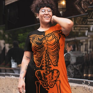 May include: A black and orange dress with a skeleton graphic print. The dress has short sleeves and a relaxed fit.