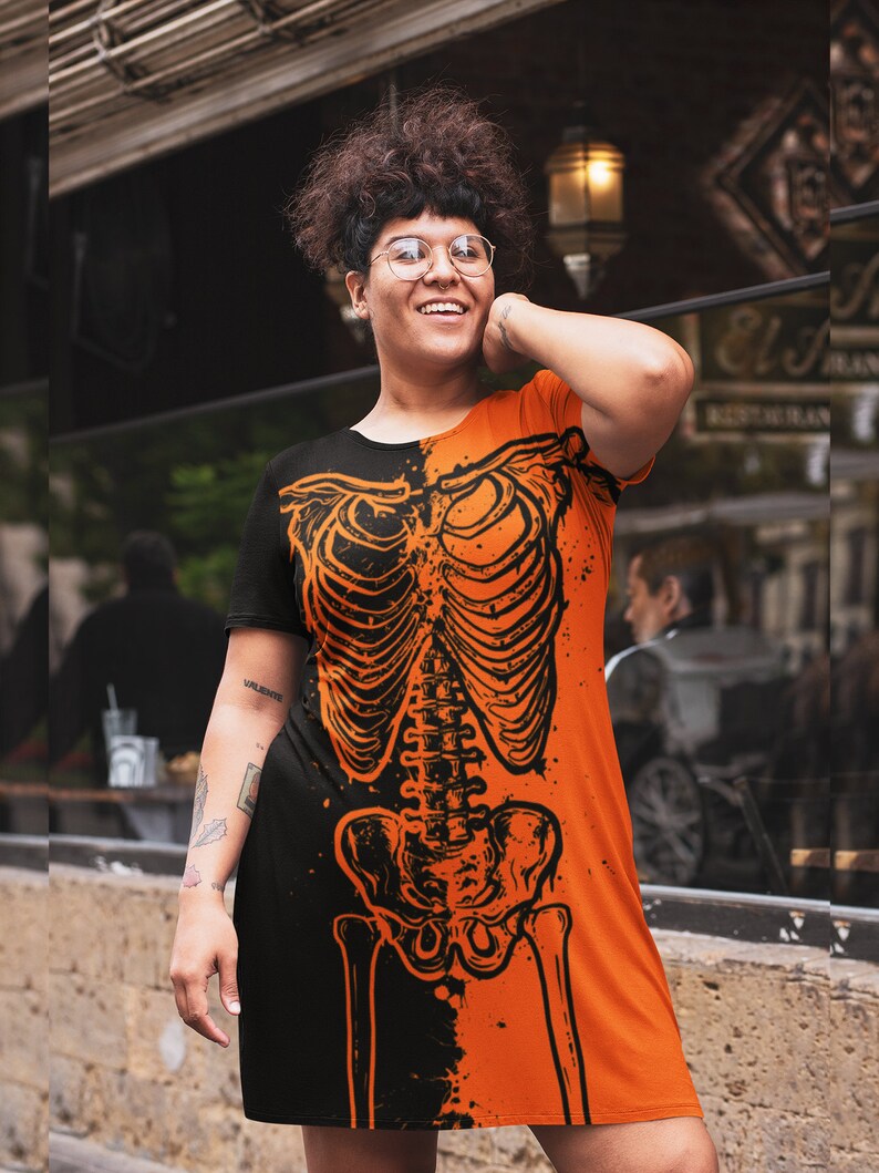 May include: A black and orange dress with a skeleton graphic print. The dress has short sleeves and a relaxed fit.