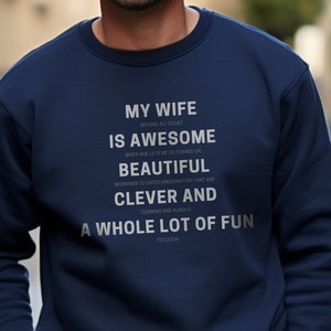 May include: Navy blue sweatshirt with a white graphic print that reads "My wife is awesome... a whole lot of fun to catch".
