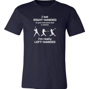 May include: Navy blue t-shirt with a white graphic of three baseball players. The text reads "I bat RIGHT-HANDED to give everyone else a chance. I'm really LEFT-HANDED."