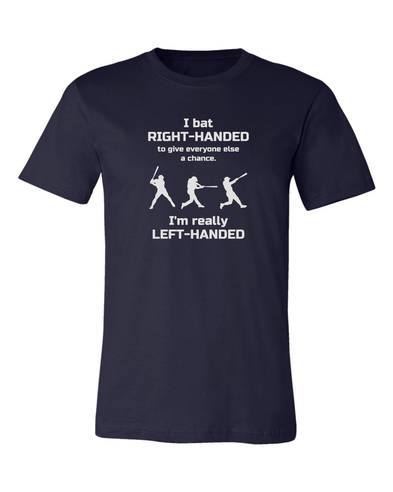 May include: Navy blue t-shirt with a white graphic of three baseball players. The text reads "I bat RIGHT-HANDED to give everyone else a chance. I'm really LEFT-HANDED."