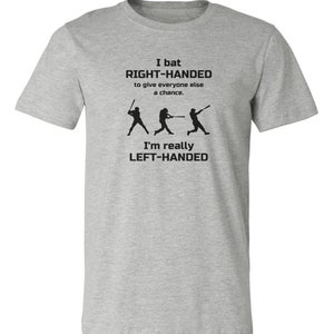 May include: Gray t-shirt with a baseball-themed design. The text reads "I bat RIGHT-HANDED to give everyone else a chance. I'm really LEFT-HANDED".
