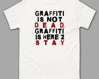 May include: White t-shirt with black text that reads "GRAFFITI IS NOT DEAD GRAFFITI IS HERE 2 STAY". The text is in a distressed font style with some letters in red.