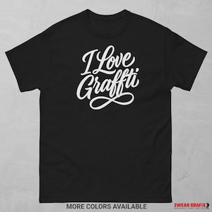 Könnte beinhalten: Schwarzes T-Shirt mit dem weißen Schriftzug "I Love Graffiti" in einer kursiven Schriftart. Das Shirt hat kurze Ärmel und einen Rundhalsausschnitt. Der untere Teil des Shirts trägt den Text "MORE COLORS AVAILABLE".