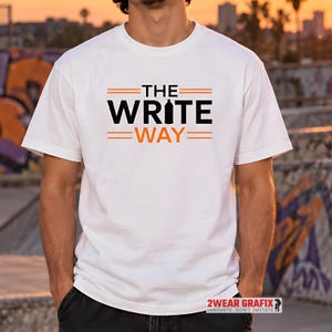 Könnte beinhalten: Ein weißes Kurzarm-T-Shirt mit dem schwarzen und orangefarbenen Schriftzug THE WRITE WAY, bei dem der Buchstabe I durch ein Sprühdosen-Symbol ersetzt wurde, flankiert von horizontalen orangefarbenen Linien über und unter dem Text.