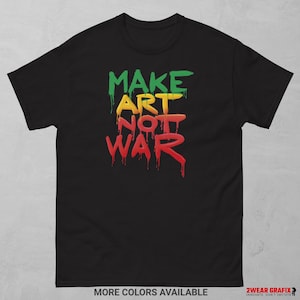 Puede incluir: Camiseta negra con la frase "MAKE ART NOT WAR" en letras verdes, amarillas y rojas goteando. La camiseta también tiene el texto "MORE COLORS AVAILABLE" en la parte inferior.