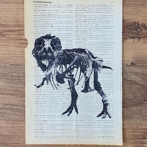 May include: A black and white dinosaur skeleton illustration is printed on a vintage dictionary page. The image is a unique blend of art and literature, perfect for a home decor piece. The page is slightly torn, adding to its antique charm.