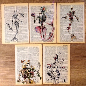 May include: Five vintage book pages featuring hand-drawn illustrations of skeletons with floral and mermaid details. The skeletons are drawn in black ink and the flowers are in shades of pink, red, and yellow. The mermaids have blue and pink tails.