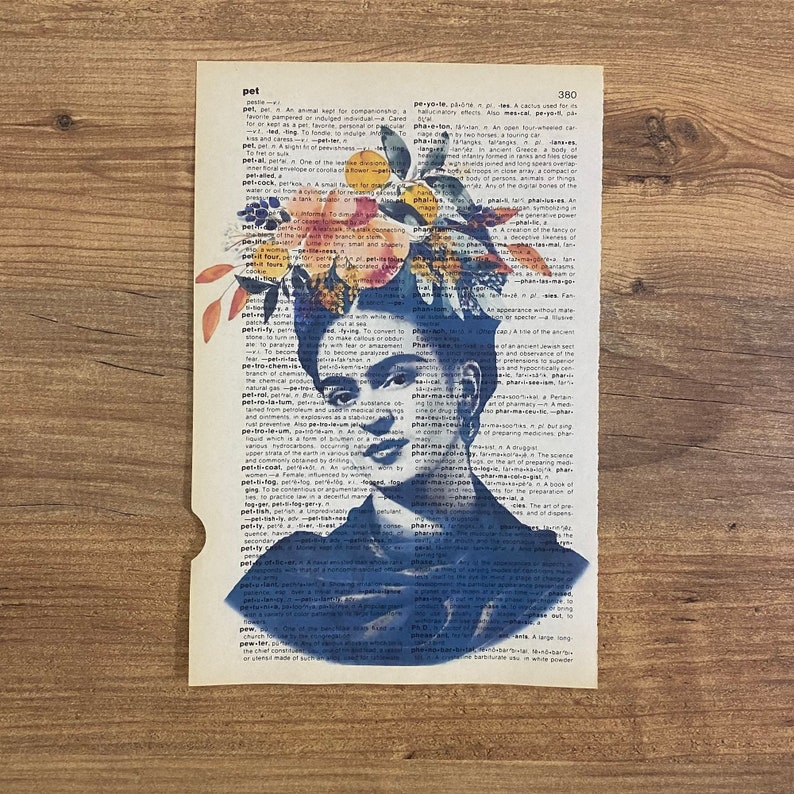 Op de afbeelding: Een blauw en wit portret van Frida Kahlo met een bloemenkrans op haar hoofd. Het portret is over een pagina uit een woordenboek gelegd, waarbij het woord "pet" is gemarkeerd.