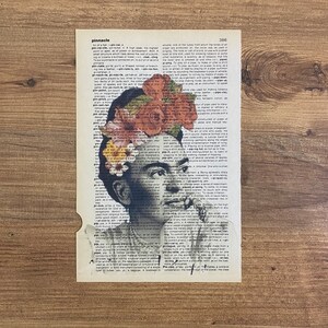 Op de afbeelding: Een zwart-wit portret van Frida Kahlo met bloemen op haar hoofd. Het portret is afgedrukt op een pagina uit een woordenboek met het woord "pinnacle" gemarkeerd.