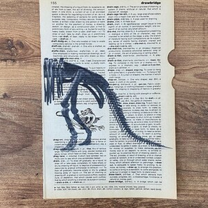 May include: A vintage dictionary page with a black dinosaur skeleton illustration and the word "dragon" below. The page is torn on the right side, and the text is visible.