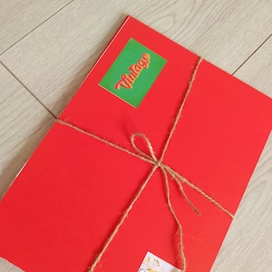 Op de afbeelding: Een rood pakketje gebonden met touw en versierd met twee stickers. E&eacute;n sticker zegt "Vintage" in een retro-lettertype en de andere zegt "Dear Paper" met een bloemenmotief.